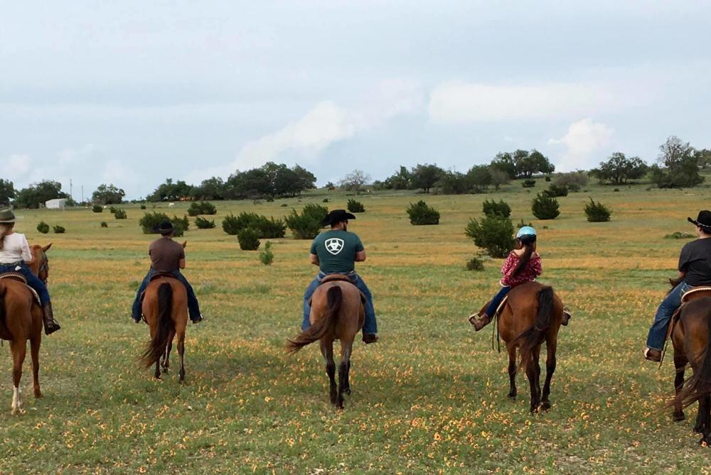 Horseback riders cross a field with Bit and Bridle Stables in Fredericksburg, TX