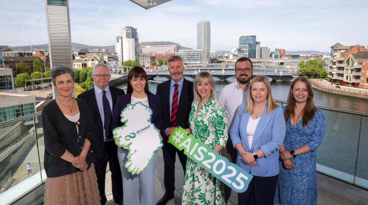 People in Belfast on a balcony holding a sign for the All-Ireland Sustainability Summit and expo.