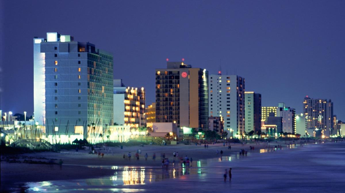 Nighttime photo of Myrtle Beach showing hotel windows lit up with small numbers of people gathered along the beach