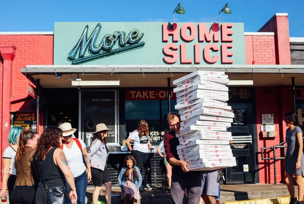 Person walking away from the line with a tall stack of pizza boxes at More Home Slice