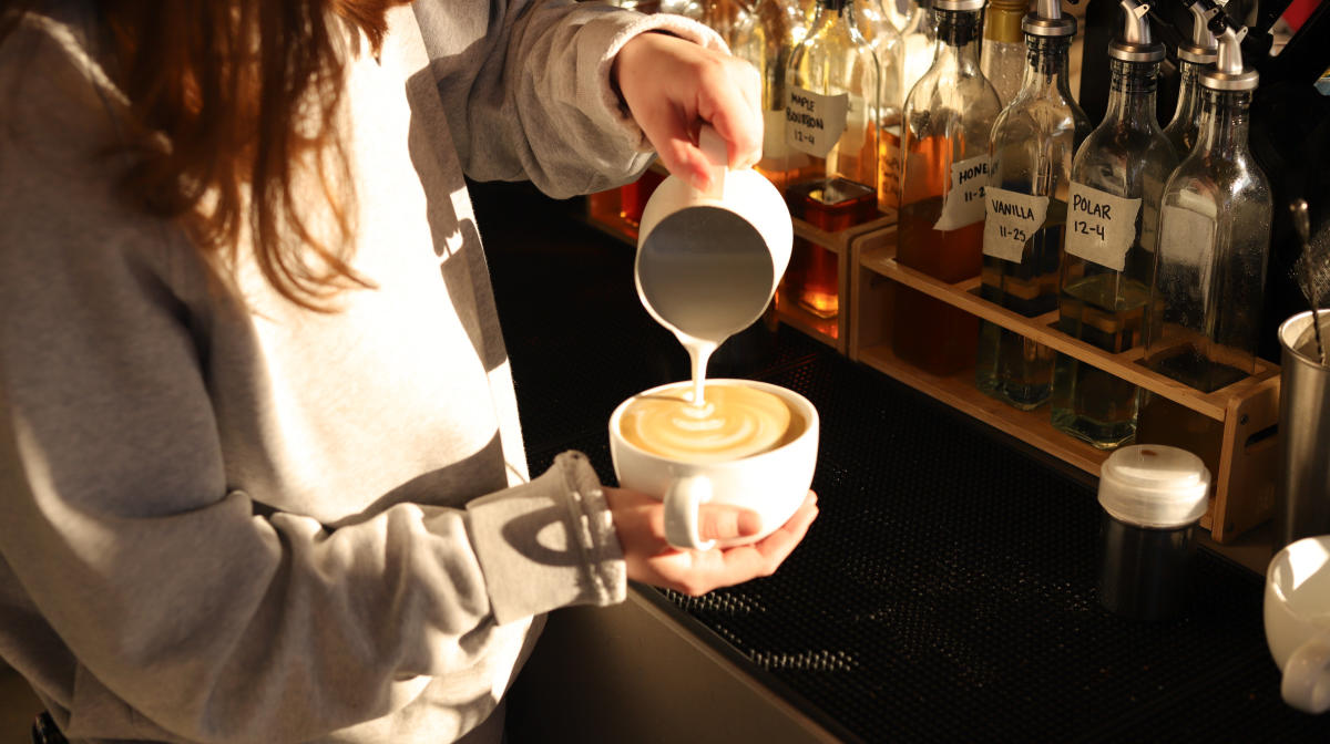 A barista pours hot milk in a cup of coffee at Cofellow.