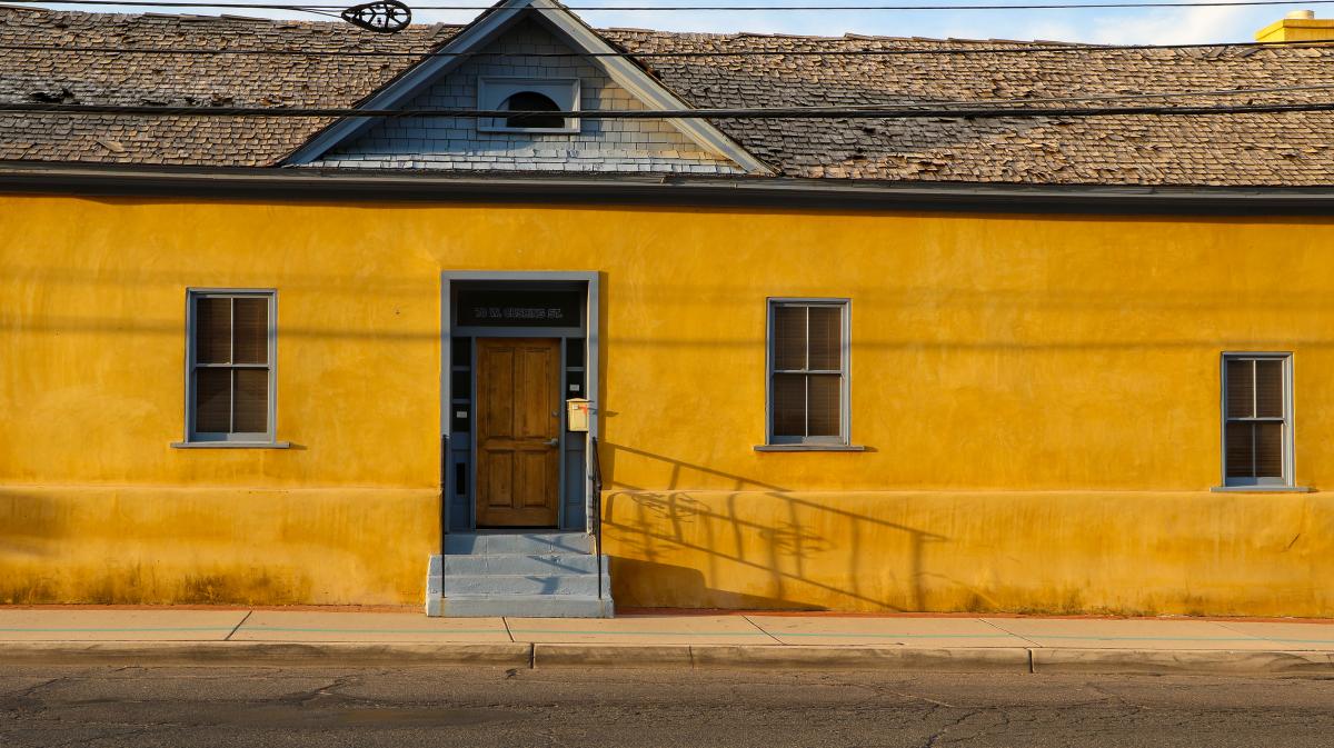 Photo of bright yellow house with blue shutters and wood door in the Historic Barrio Viejo Neighborhood