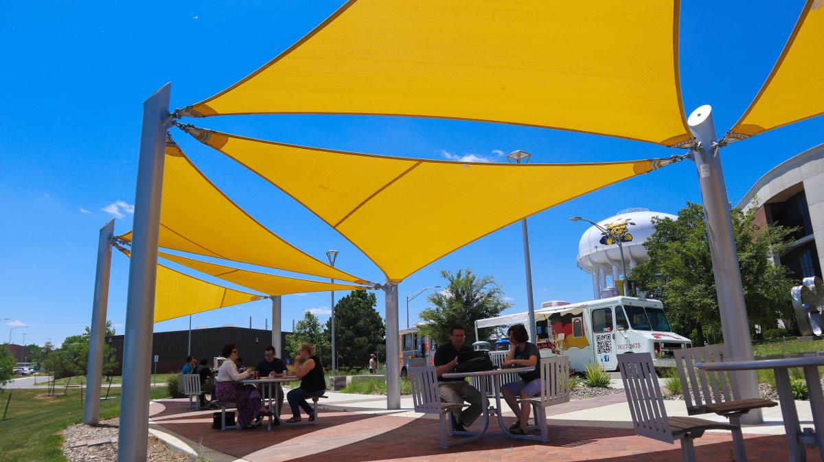 People sit and eat under the shade at the food truck plaza on the campus of Wichita State University
