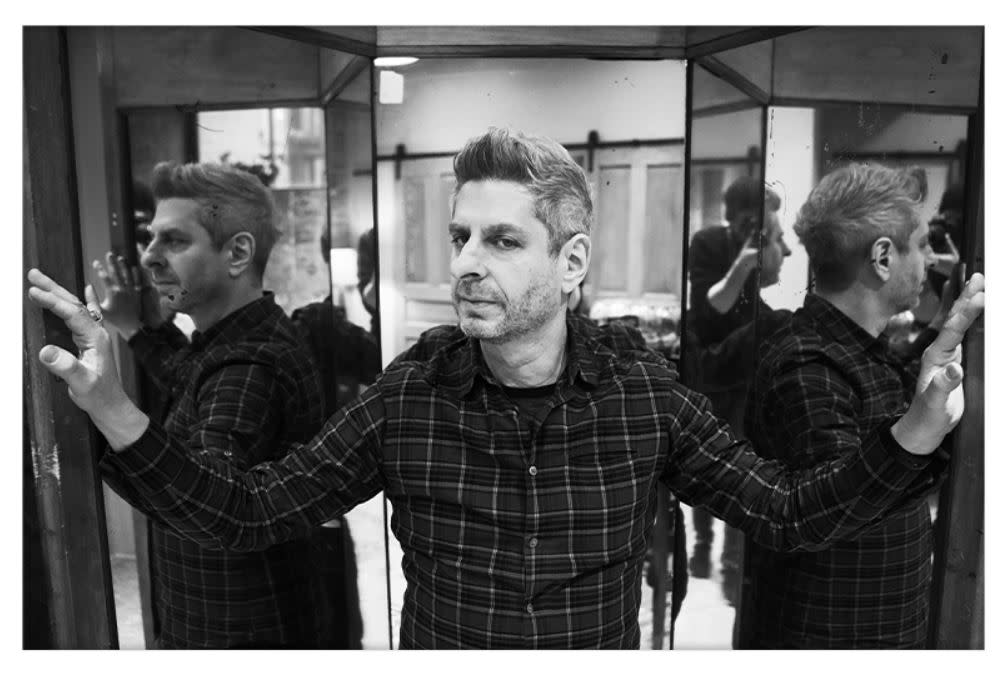 Image is of Mike Gordon standing next to a mirror which show's Mike from 3 angles.