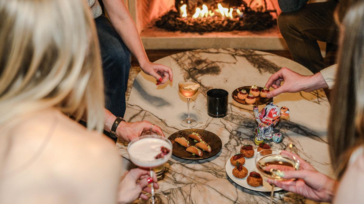 Image of people reaching for appetizers sitting on a central marble table.