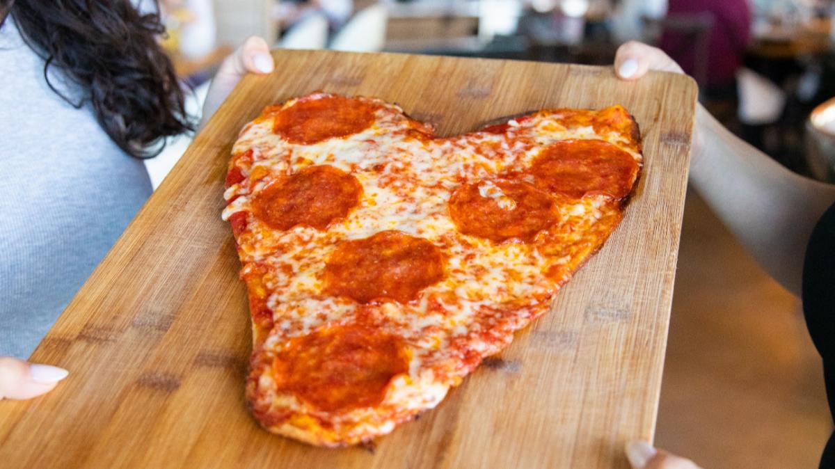 a heart shaped pepperoni pizza on a cutting board