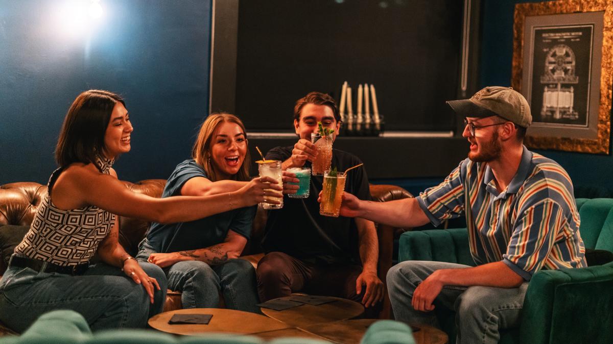 Four people cheers-ing at seating area in Looking Glass Escape Lounge