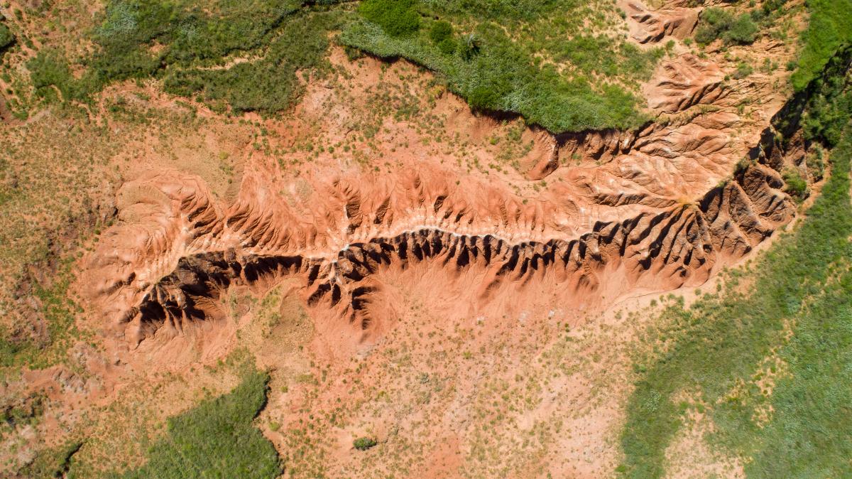 Looking down at a rugged landscape of red hills that looks like a spine. Patchy green grass surrounds the hills