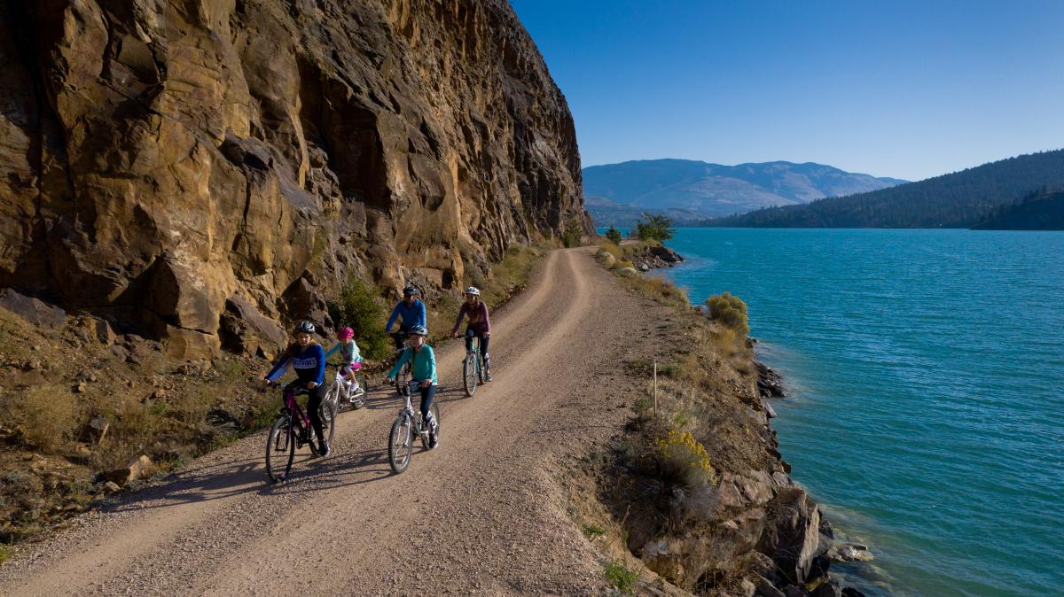 A family riding bikes on a trail next to a lake