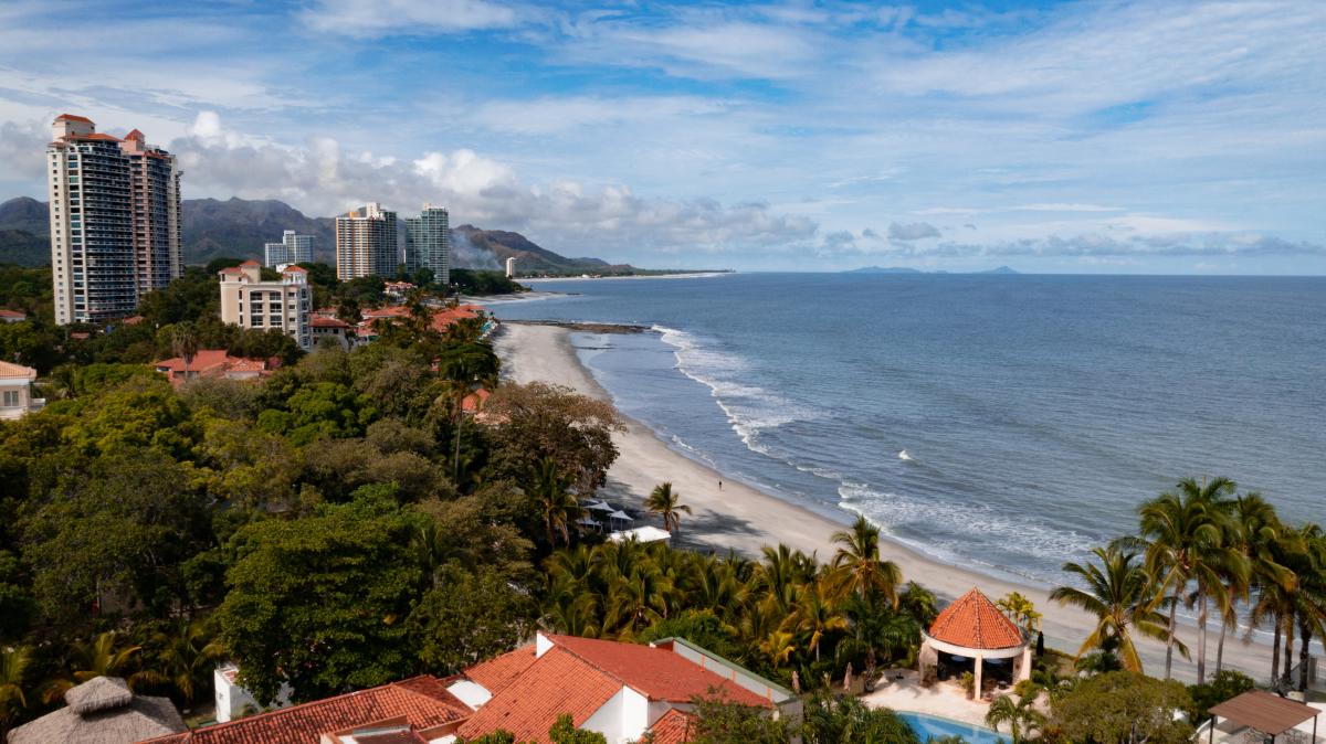 Una vista panorámica de la playa de Coronado, Panamá, con una orilla de arena blanca, océano azul y una línea de edificios altos en la distancia.