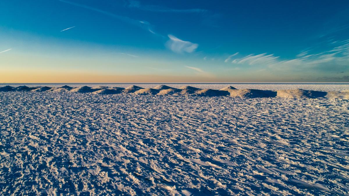 Snow and ice reach to the horizon. A blue sky is overhead with a tint of orange near the skyline.