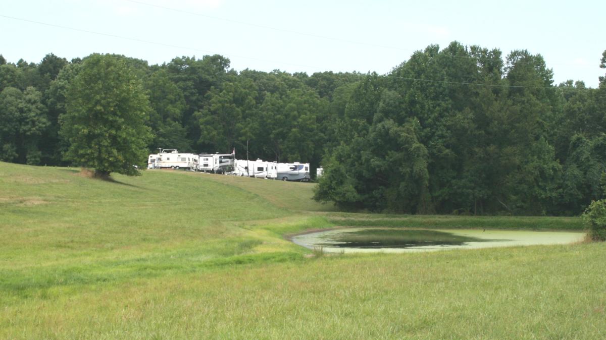 a field with trees and campers/recreational vehicles in the distance