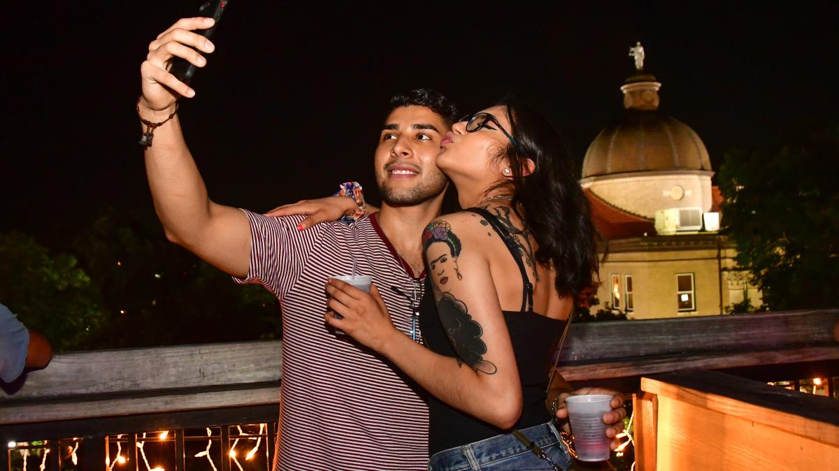 Couple taking selfie on rooftop bar with courthouse in background