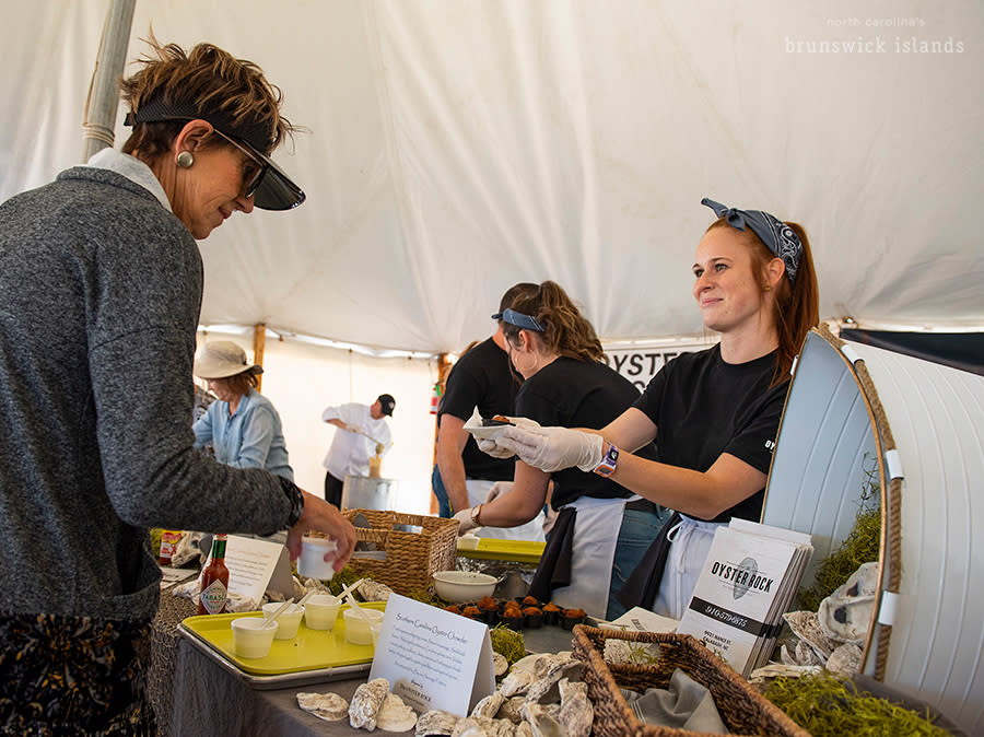 a woman handing a customer a cup of oyster stew