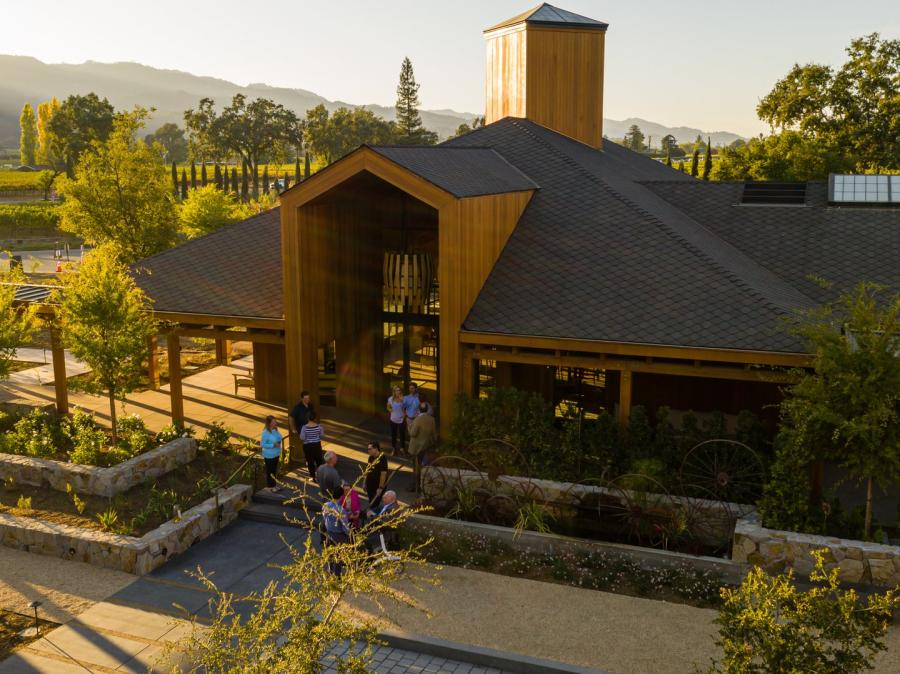 A wooden winery building surrounded by landscaped gardens and vineyards in Napa Valley at sunset.