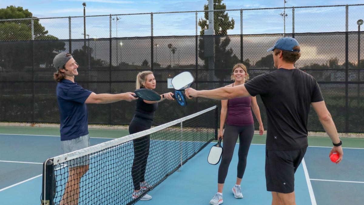 Four people gather near the center of a pickleball net