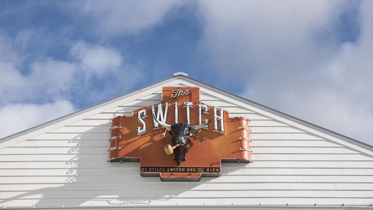 Neon sign with "The Switch" in capital letters and a bull head mounted on a white wall.