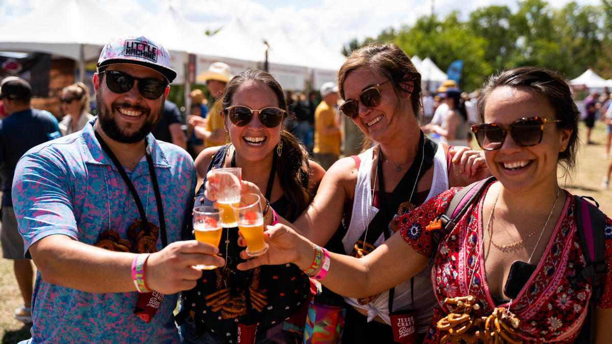 Image of four people at the Texas Craft Brewers Festival hoisting up glasses of beer in a toast while smiling at the camera.