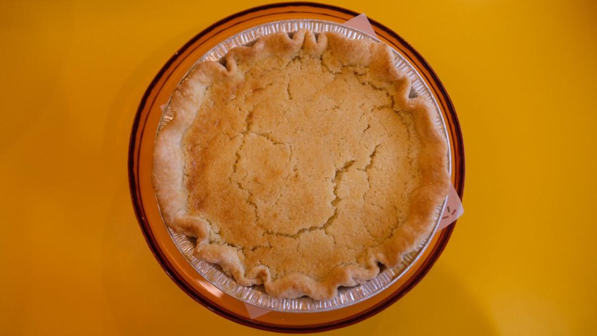 A freshly baked pie in a silver tin sits on a round amber plate against a bright yellow background, showcasing its golden crust.