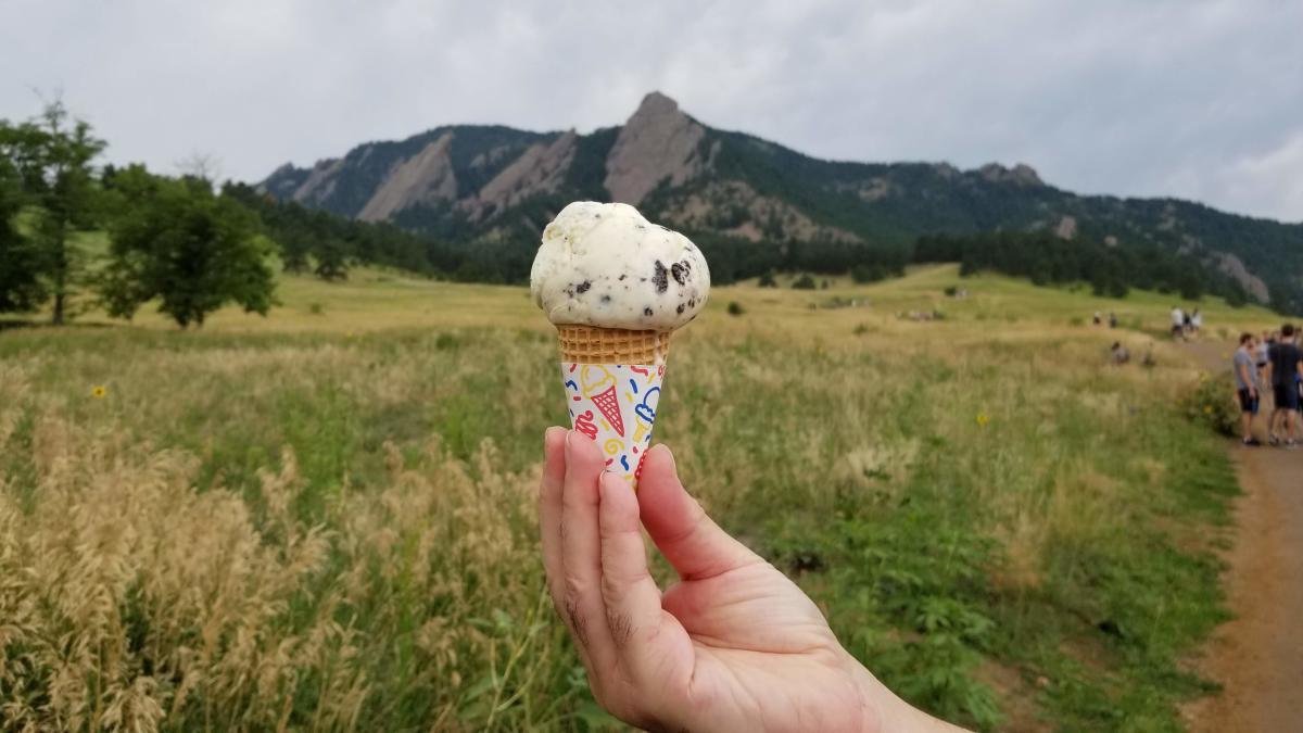 Chocolate chip ice cream cone held in front of the Flatirons in the distance
