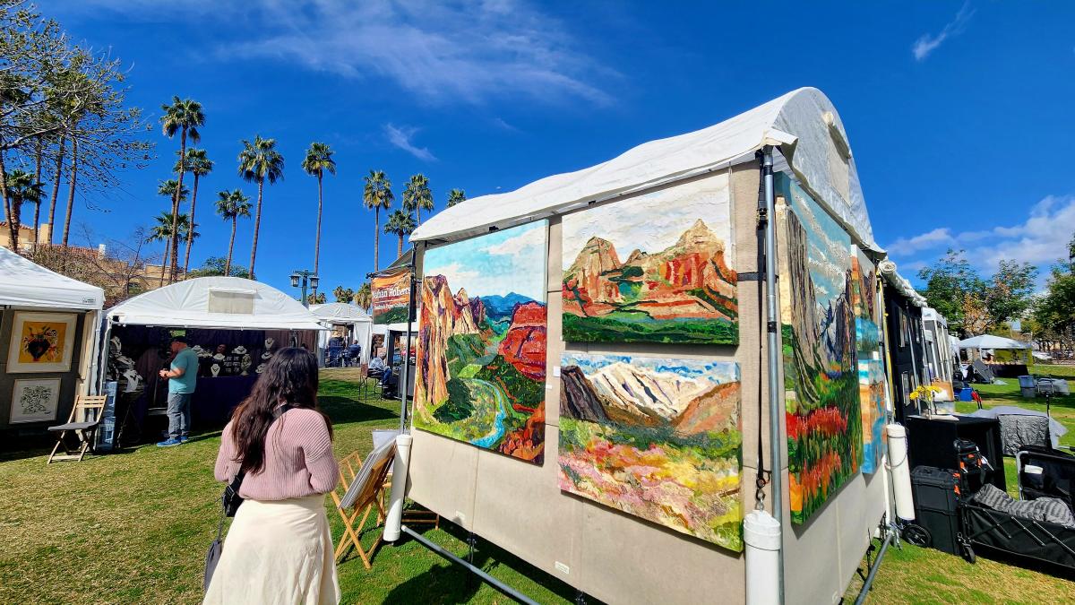 a lady looking at an artist booth at an outdoor festival with blue skies and palm trees