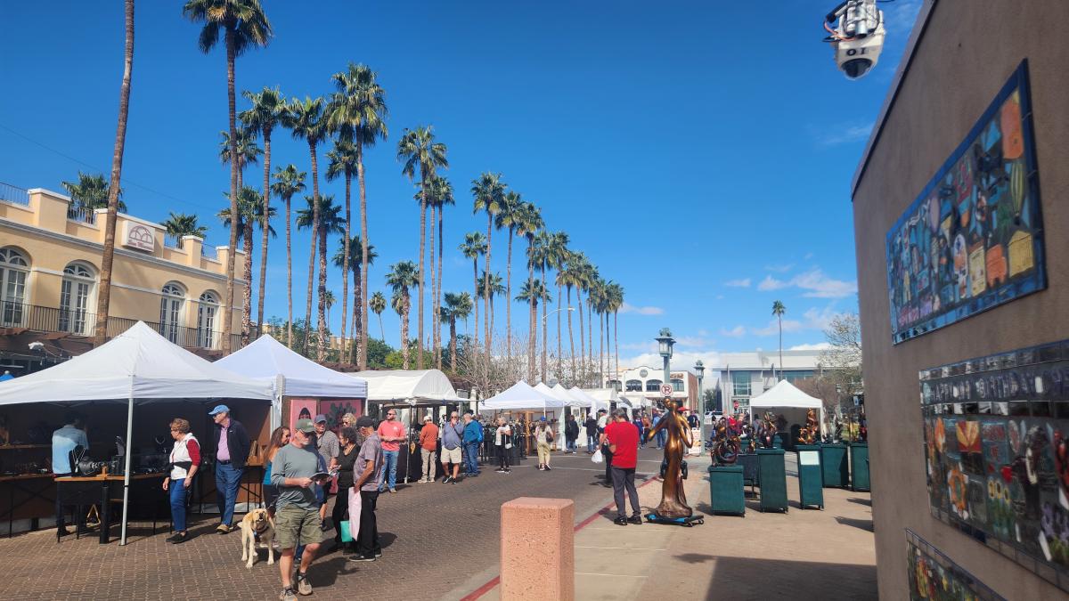 outdoor festival with booths featuring artwork on a sunny day with palm trees in the background