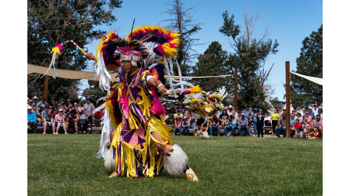 Native dancer mid-performance in colorful feathered regalia, participating in a traditional dance circle at Morning Star American Indian Village during Cheyenne Frontier Days.