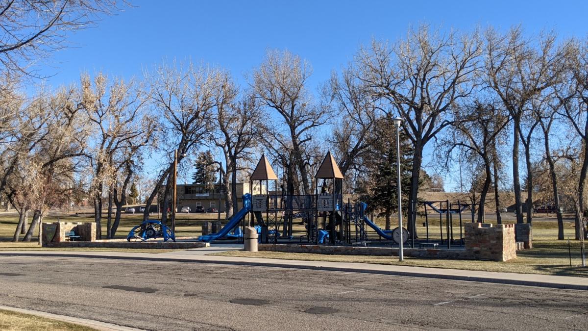 Scenic view of Holliday Park in Cheyenne, showcasing greenery, playground equipment, and the stone wall with historical significance.