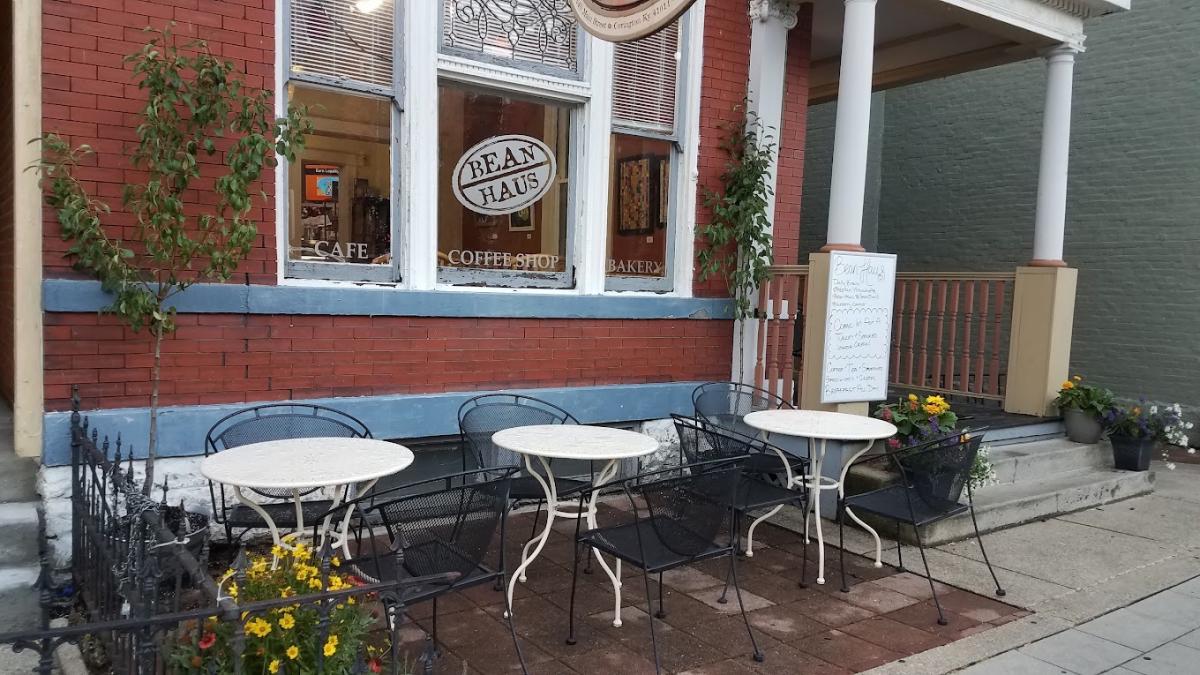 The image is of the outside facade of Bean Haus with three small white, metal tables, surrounded by black metal chairs.