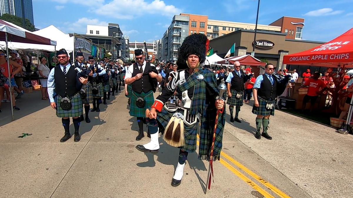 Image is of a pipping band lining up to perform in their kilts on the streets of The Banks.