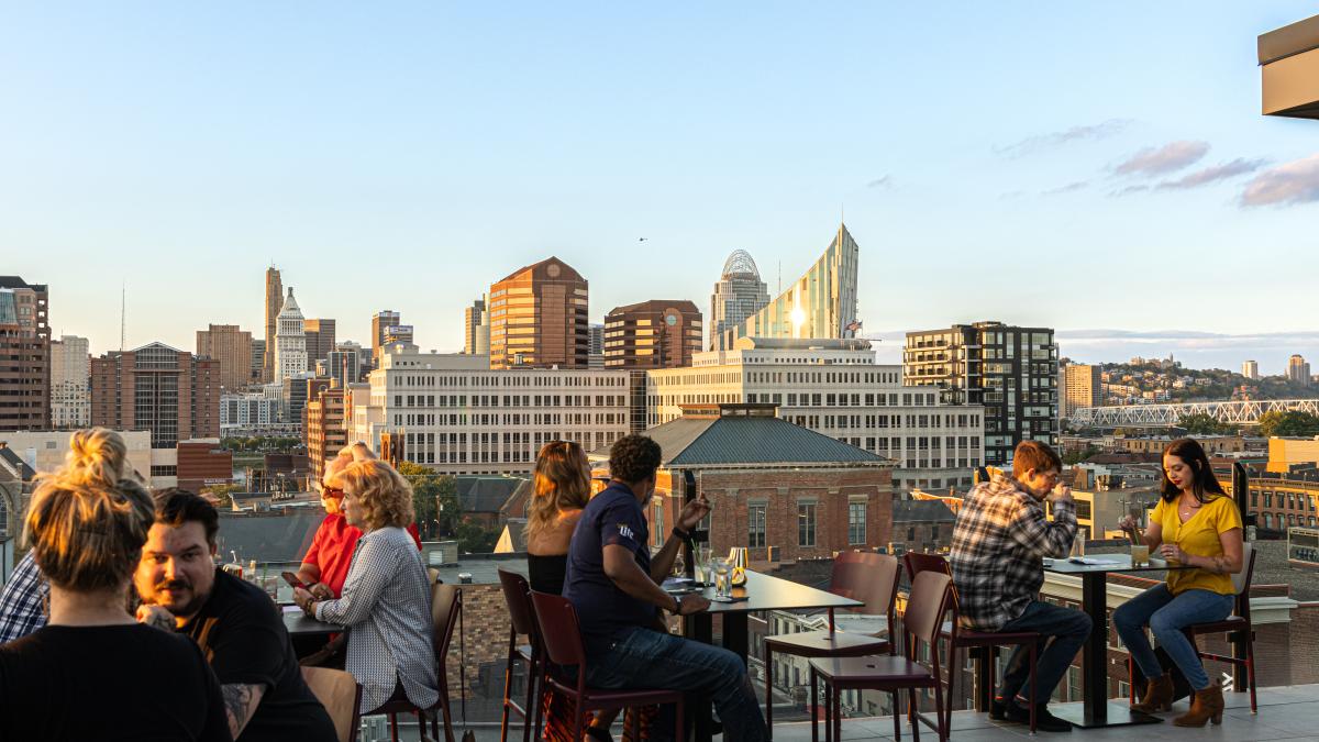 People dining at Opal rooftop restaurant with a view of the Cincinnati skyline in the background
