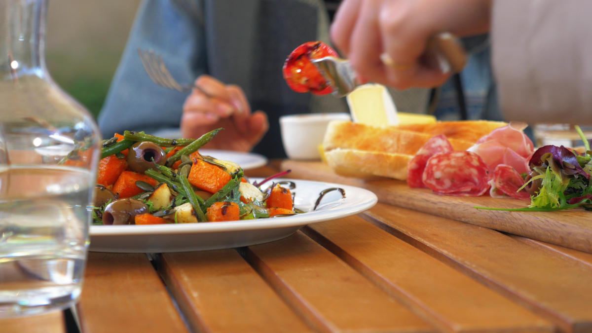 A diner enjoys a bright plate of food, including a salad and a charcuterie board.