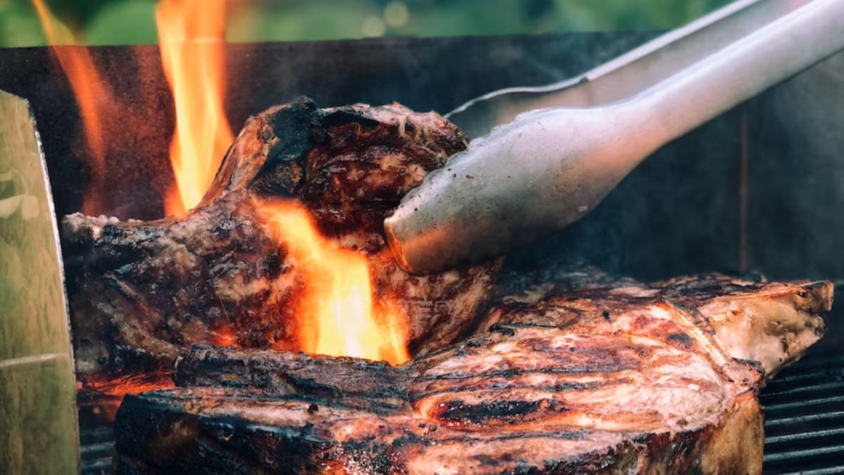 a pair of tongs flipping meat on open flame grill