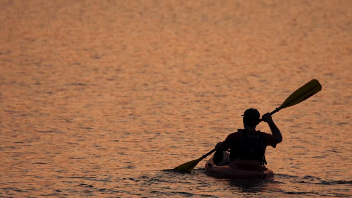 A person kayaking on Freeman Lake at sunset, with the water reflecting a warm orange glow.