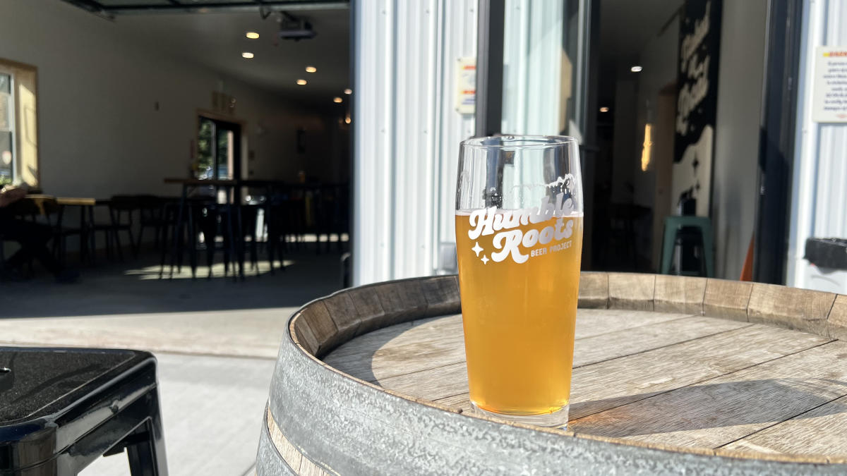 A glass of beer from Humble Roots sits on a wooden barrel outside a taproom.