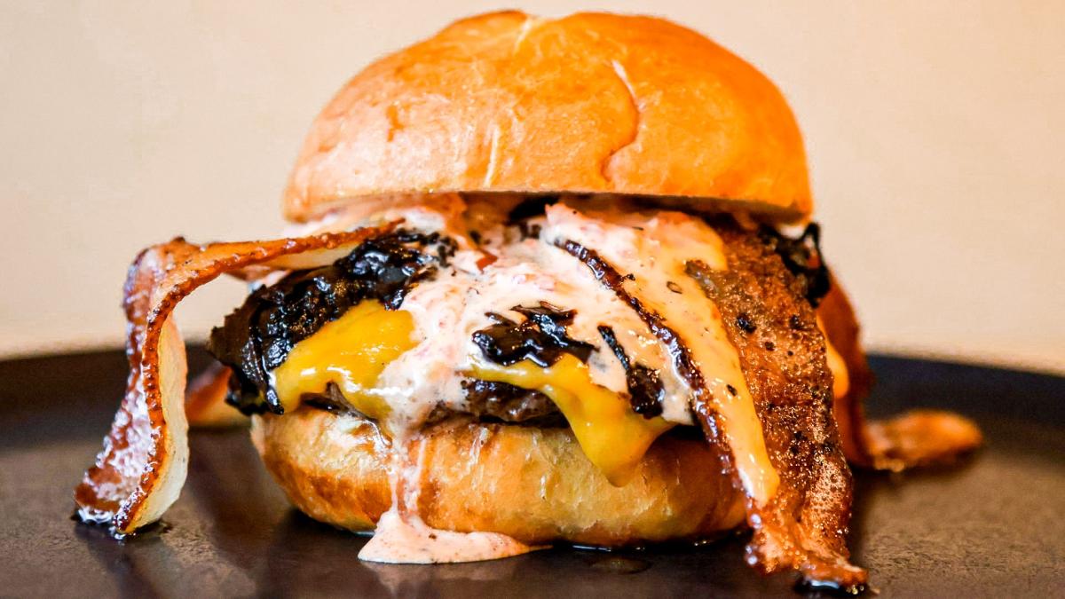 A burger with bacon, cheese, and sauce running down the side