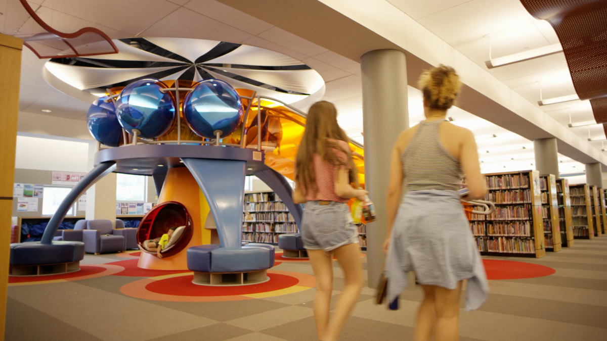 Two women walk past the reading tower in the children's section at the library. The reading tower has individual reading nooks that look like bubbles.