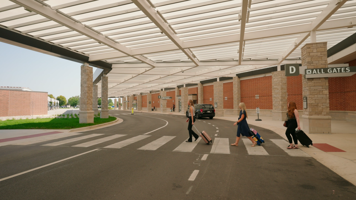 Three women walk out of FWA rolling suitcases over the curbless, wide sidewalks