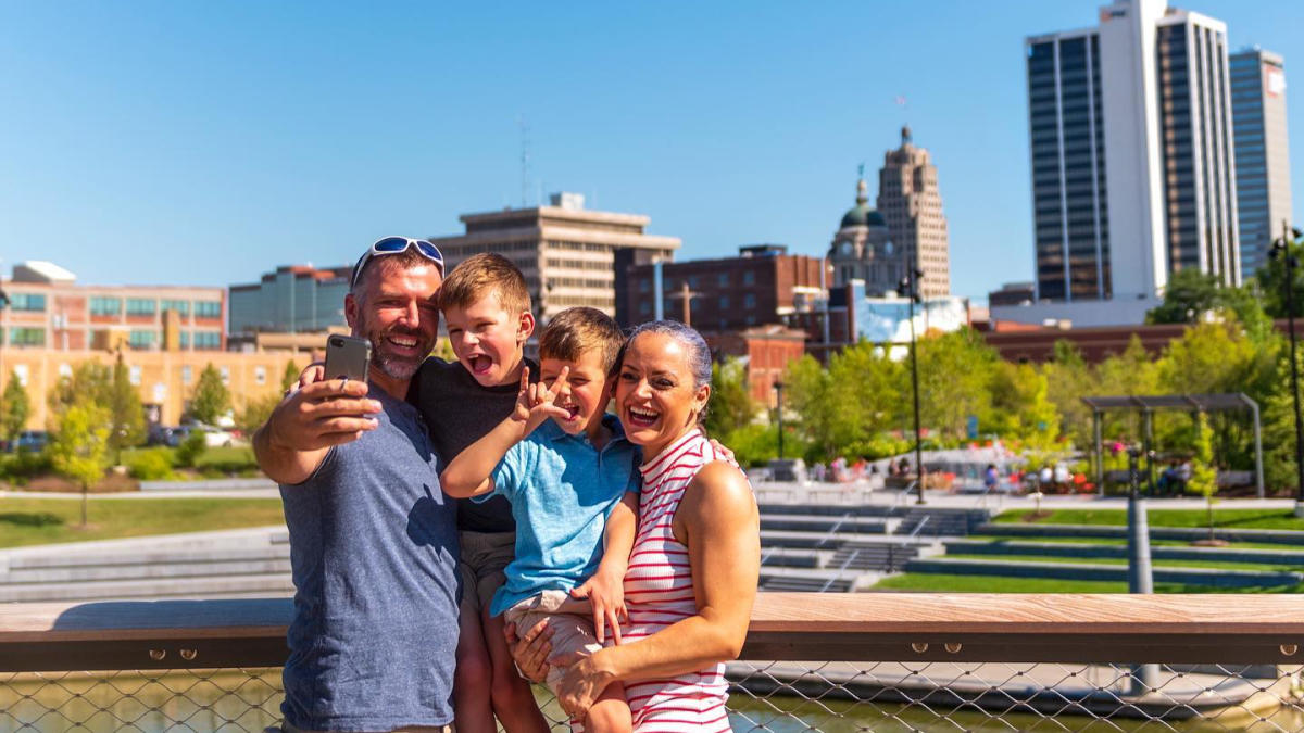 Family posing for selfie at Tree Canopy Trail in Promenade Park with skyline in background.