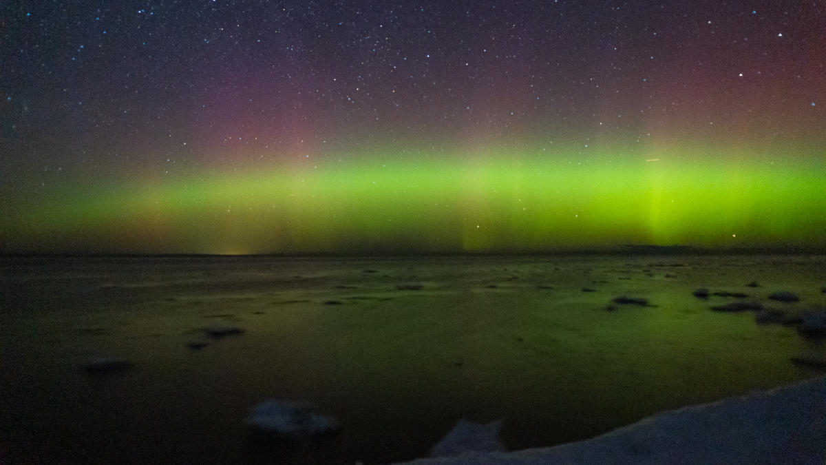 northern lights dance above a lake with floating ice