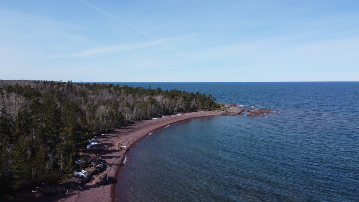 rocky shoreline studded with snowy remnants between a wide open lake and coniferous forest
