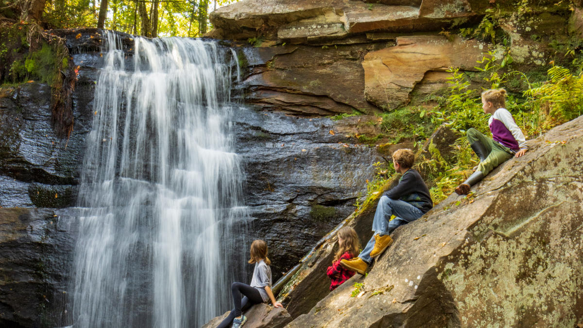 Four children sitting on a rock next to waterfall