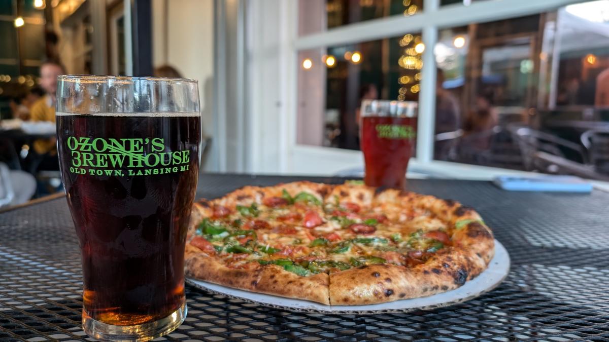 Pint of dark beer next to a pizza on a patio table