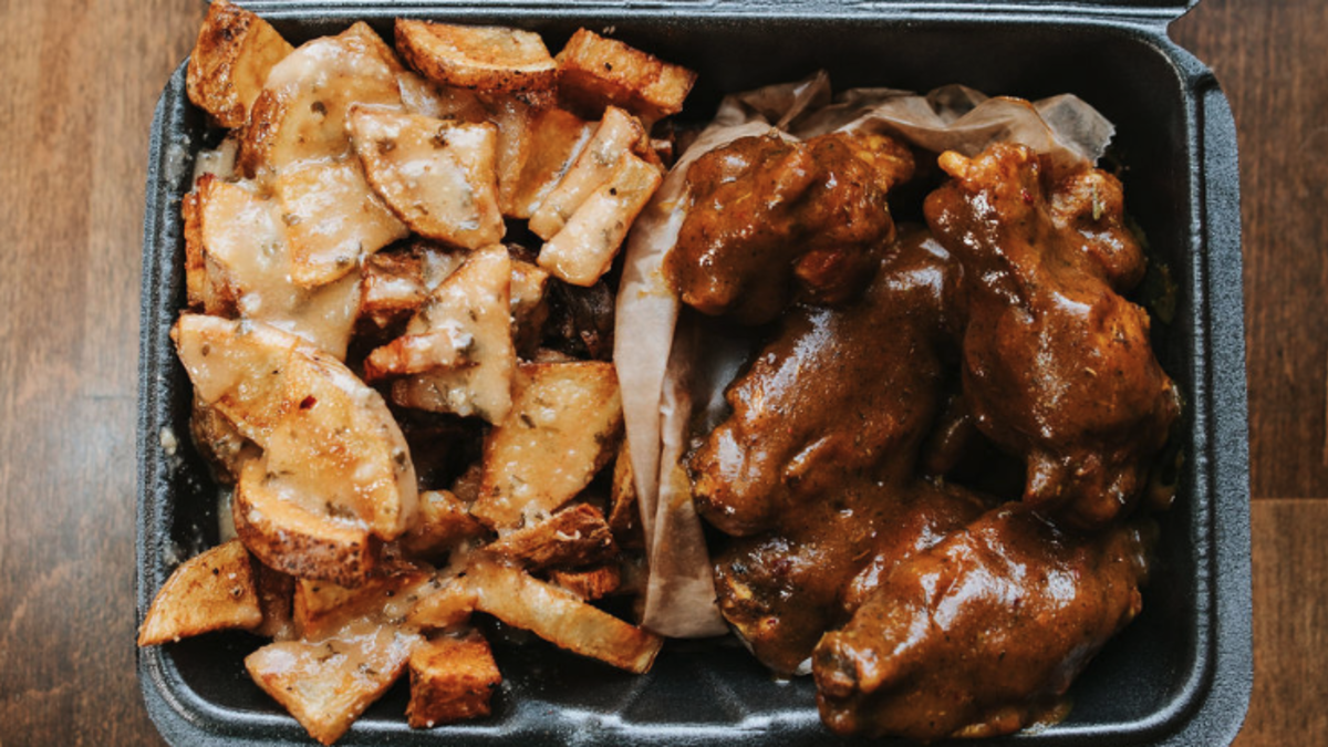 To-go box of seasoned potatoes and bone-in wings with sauce