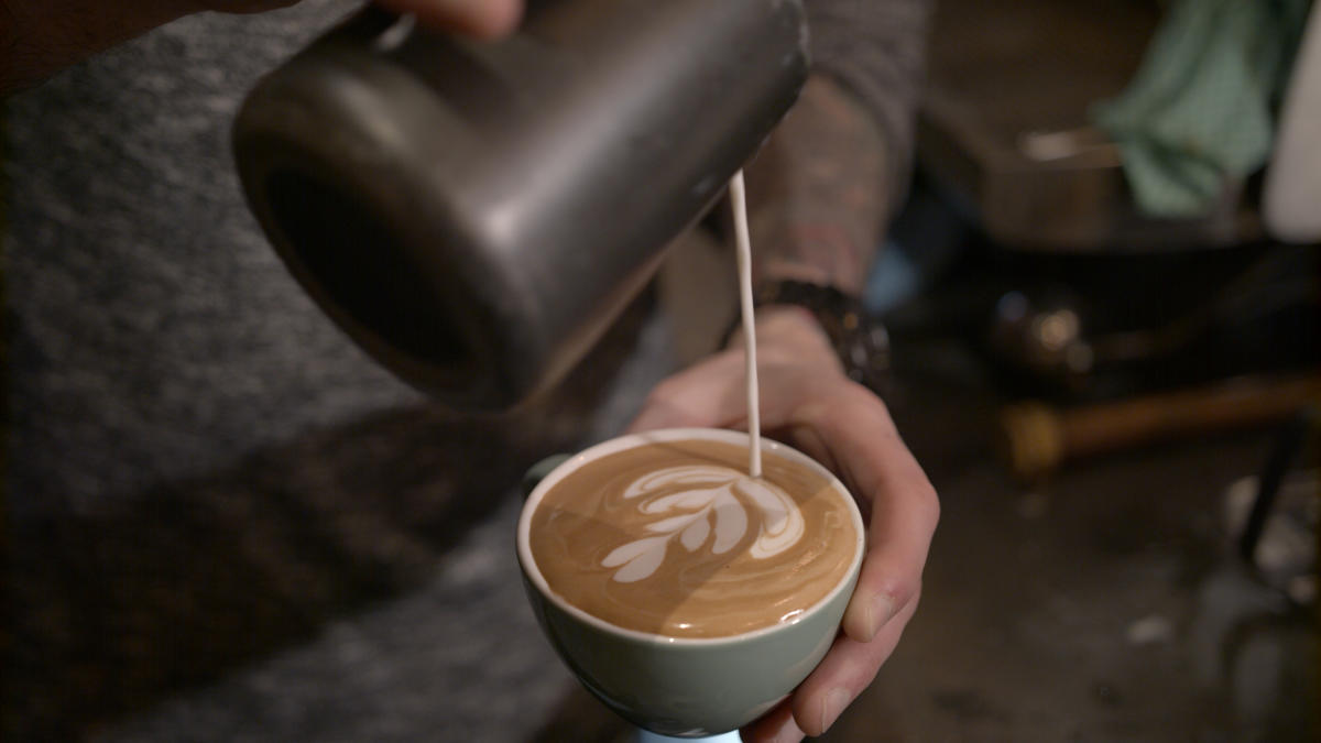 Milk being poured into a full cup of coffee