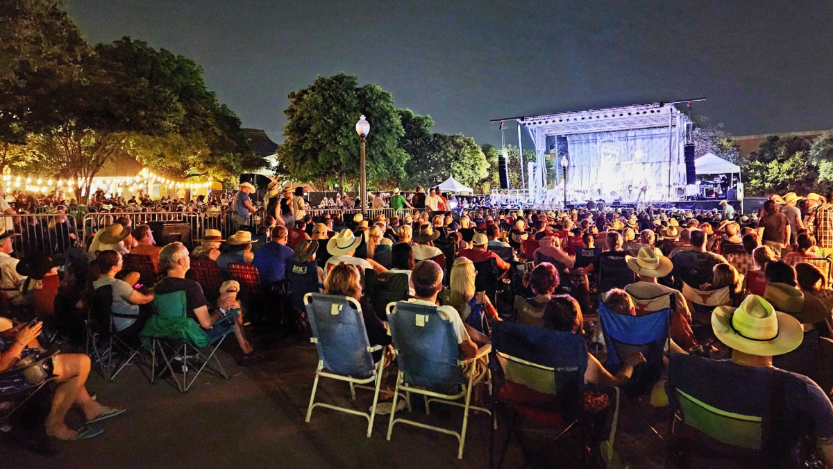 Crowd sitting in lawn chairs in front of a stage at night listening to live music