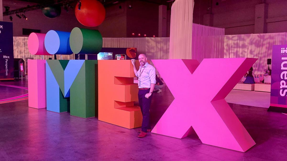 Image of worker stood next to a large sign spelling IMEX
