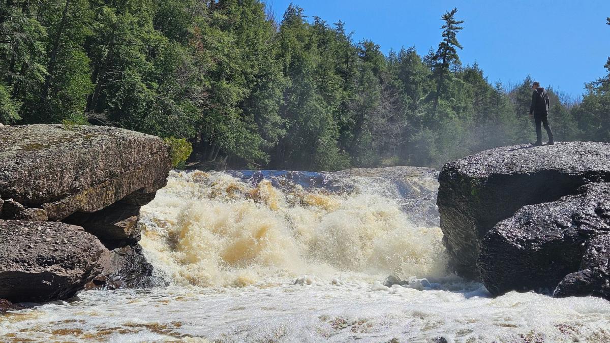 A man on a rock looking down at Sandstone Falls, a waterfall located in the Upper Peninsula of Michigan