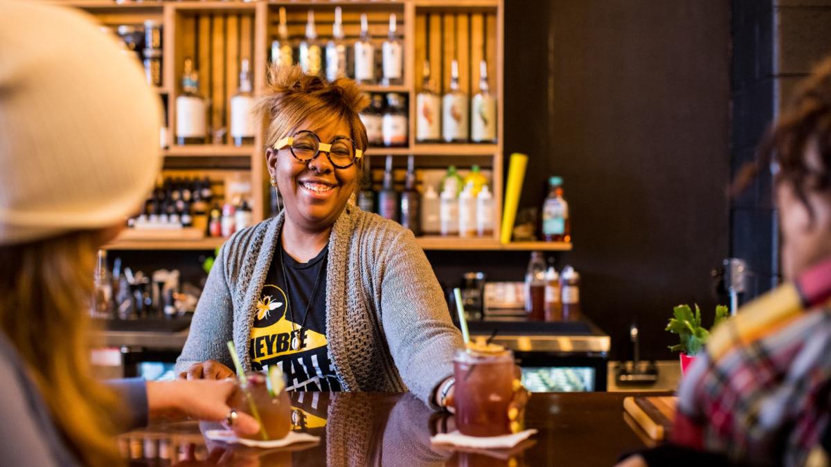 A bartender serving a non-alcoholic cocktail to two bar patrons.