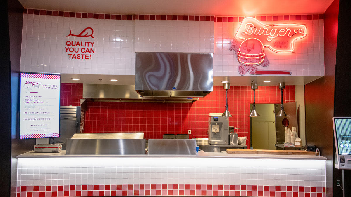 A retro-style burger counter at the Potawatomi Casino | Hotel, with red and white tile walls, stainless steel kitchen equipment, and a neon sign that reads “Burger Co.” above a cartoon burger character. A digital menu board displays featured items like cheeseburgers, chicken sandwiches, cheese curds, and milkshakes. Overhead lights and a “Quality You Can Taste!” slogan complete the nostalgic, diner-inspired look.